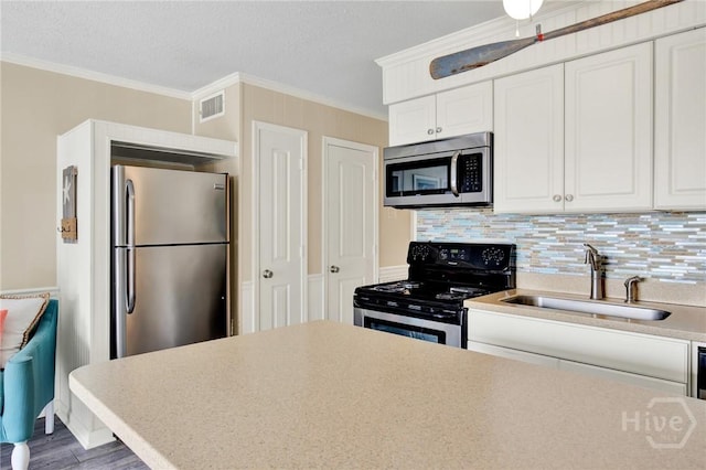 1217 Bay St Unit 105B, Tybee Island, GA 31328 - kitchen featuring appliances with stainless steel finishes, crown molding, white cabinets, wood finished floors, and light countertops