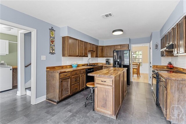 67 Oak Side Ct, Richmond Hill, GA 31324 - kitchen featuring butcher block counters, washer / clothes dryer, black appliances, a kitchen island, and backsplash