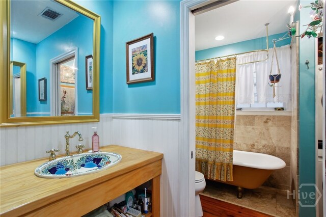 539 E Gwinnett St, Savannah, GA 31401 - full bathroom with a freestanding bath, toilet, a wainscoted wall, wood finished floors, and a shower with shower curtain