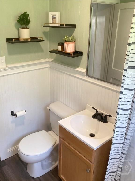 155 Oak Hill Rd, Richmond Hill, GA 31324 - bathroom with toilet, vanity, wainscoting, wood finished floors, and a decorative wall
