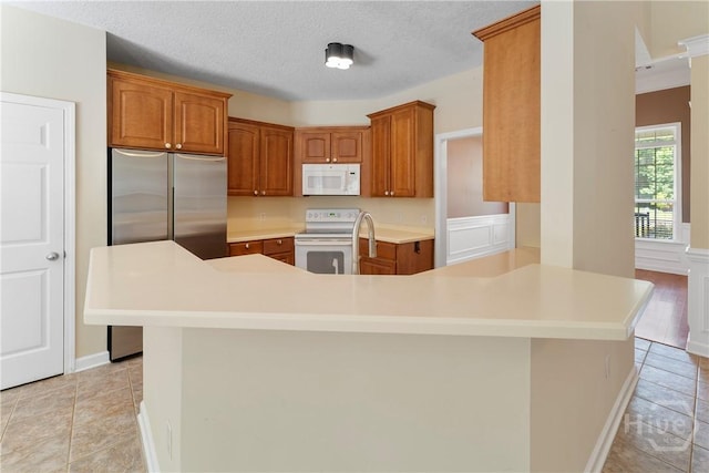 201 Henderson Oaks Dr, Savannah, GA 31419 - kitchen featuring white appliances, a peninsula, brown cabinetry, light countertops, and light tile patterned flooring