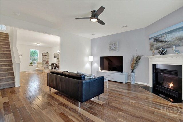 106 Tanzania Trl, Pooler, GA 31322 - living room with stairway, wood finished floors, a ceiling fan, a glass covered fireplace, and baseboards
