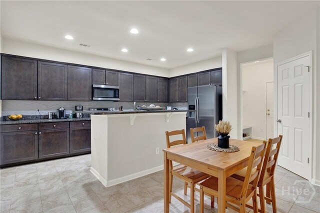106 Tanzania Trl, Pooler, GA 31322 - kitchen featuring appliances with stainless steel finishes, a breakfast bar area, dark brown cabinets, tasteful backsplash, and a center island