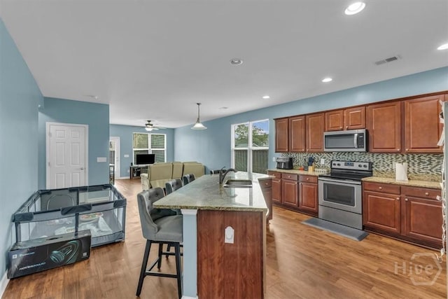 413 Lions Den Dr, Pooler, GA 31322 - kitchen with stainless steel appliances, a sink, a kitchen bar, light wood finished floors, and decorative backsplash