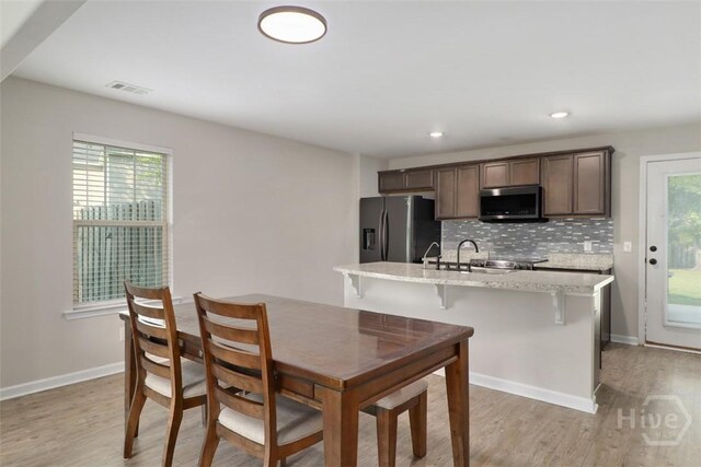 304 Boomer Ct, Guyton, GA 31312 - kitchen with appliances with stainless steel finishes, light wood-type flooring, tasteful backsplash, an island with sink, and a kitchen bar