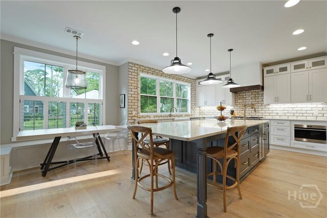 315 Linkside Lake Dr, Richmond Hill, GA 31324 - kitchen featuring oven, tasteful backsplash, a center island with sink, white cabinetry, and glass insert cabinets