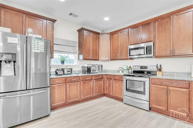 194 Calm Oaks Cir, Savannah, GA 31419 - kitchen featuring appliances with stainless steel finishes, light stone counters, light wood-style floors, brown cabinetry, and recessed lighting