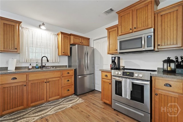 152 Covey Rise Pl, Midway, GA 31320 - kitchen with appliances with stainless steel finishes, a sink, light wood-type flooring, dark countertops, and brown cabinetry