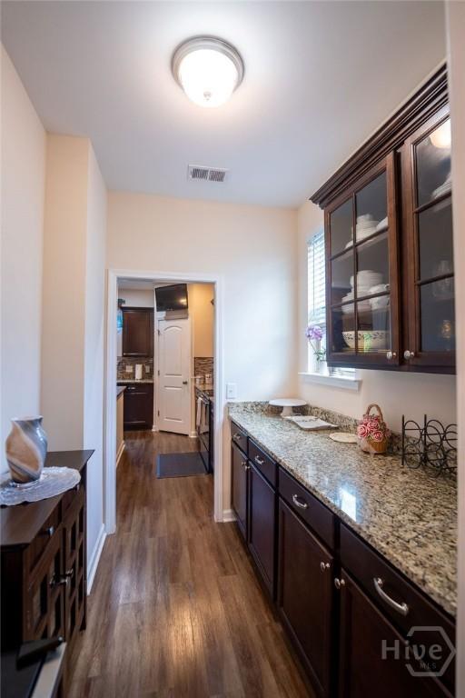 66 Tarbert Cut Cut, Richmond Hill, GA 31324 - kitchen featuring dark brown cabinetry, dark wood-type flooring, light stone countertops, and glass insert cabinets