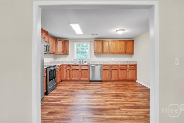 142 Bill Brown Rd, Pembroke, GA 31321 - kitchen featuring stainless steel appliances, light wood-type flooring, brown cabinetry, and light stone counters