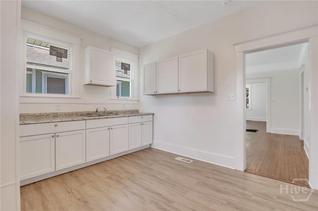 521 Seiler Ave, Savannah, GA 31401 - kitchen with light wood-type flooring, white cabinetry, light stone countertops, baseboards, and a sink
