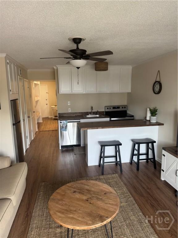 1217 Bay St Unit 105A, Tybee Island, GA 31328 - kitchen with appliances with stainless steel finishes, dark countertops, a ceiling fan, a textured ceiling, and white cabinetry