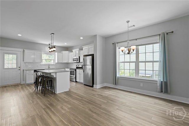 623 E Henry St, Savannah, GA 31401 - kitchen with appliances with stainless steel finishes, a chandelier, white cabinetry, light wood-style floors, and a kitchen breakfast bar