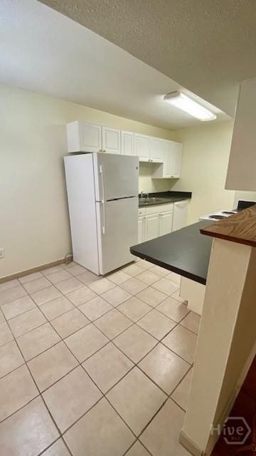 401 N Cromwell Rd Unit G1, Savannah, GA 31410 - kitchen with freestanding refrigerator, dark countertops, light tile patterned floors, white cabinets, and a peninsula