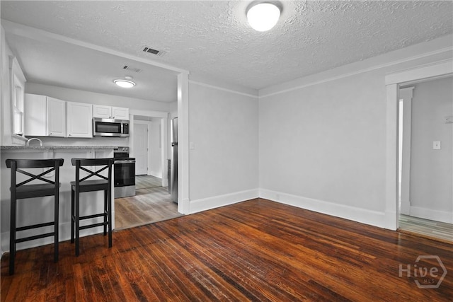 1122 SE 36th St, Savannah, GA 31404 - kitchen with appliances with stainless steel finishes, white cabinetry, wood finished floors, a textured ceiling, and a kitchen breakfast bar