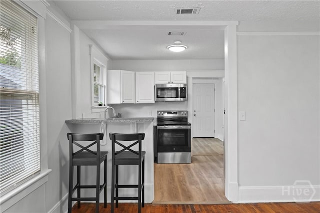 1122 SE 36th St, Savannah, GA 31404 - kitchen with stainless steel appliances, white cabinets, a breakfast bar, plenty of natural light, and a textured ceiling