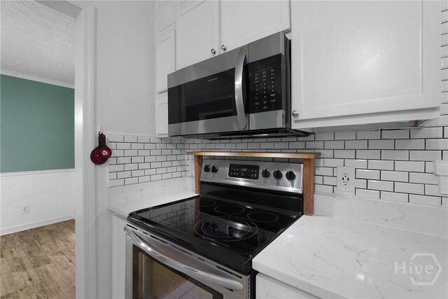75 Brown Thrasher Ct, Richmond Hill, GA 31324 - kitchen featuring stainless steel appliances, white cabinetry, light wood-style flooring, wainscoting, and crown molding