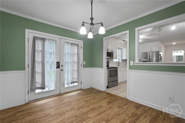75 Brown Thrasher Ct, Richmond Hill, GA 31324 - unfurnished dining area featuring french doors, a wainscoted wall, light wood-style flooring, a chandelier, and a textured ceiling