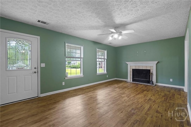 75 Brown Thrasher Ct, Richmond Hill, GA 31324 - unfurnished living room with plenty of natural light, wood finished floors, a tiled fireplace, ceiling fan, and a textured ceiling