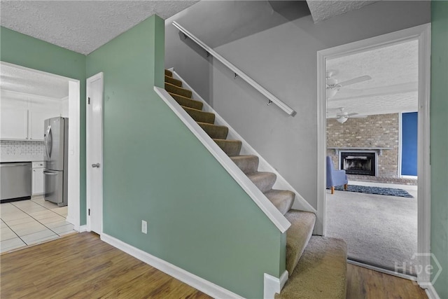 75 Brown Thrasher Ct, Richmond Hill, GA 31324 - stairs with a textured ceiling, a ceiling fan, wood finished floors, and a brick fireplace
