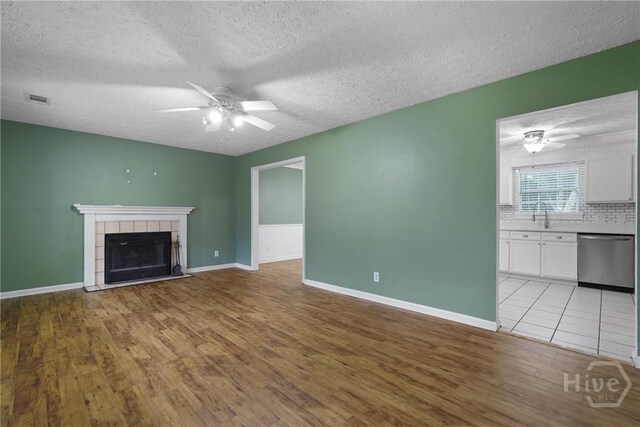 75 Brown Thrasher Ct, Richmond Hill, GA 31324 - unfurnished living room featuring ceiling fan, light wood finished floors, a textured ceiling, and a tiled fireplace