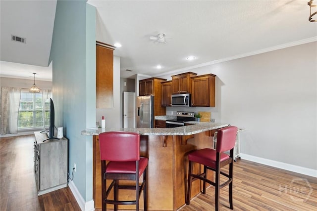 112 Kingsley Dr N, Guyton, GA 31312 - kitchen featuring appliances with stainless steel finishes, wood finished floors, brown cabinetry, a kitchen breakfast bar, and a peninsula