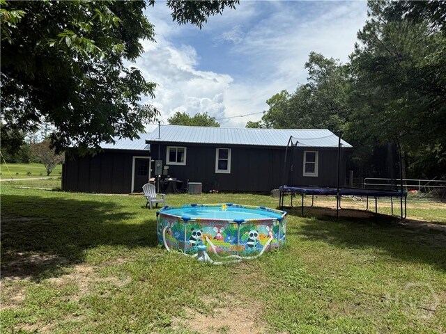 3052 Effingham Hwy, Sylvania, GA 30467 - rear view of house featuring a trampoline, a yard, board and batten siding, an outdoor pool, and a metal roof
