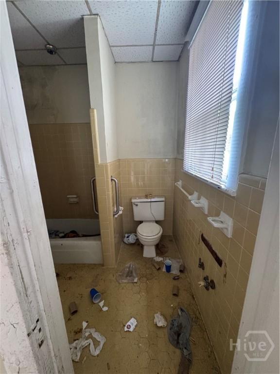 601 W 45th St, Savannah, GA 31405 - full bath with a shower with shower door, tile walls, a wainscoted wall, and a paneled ceiling