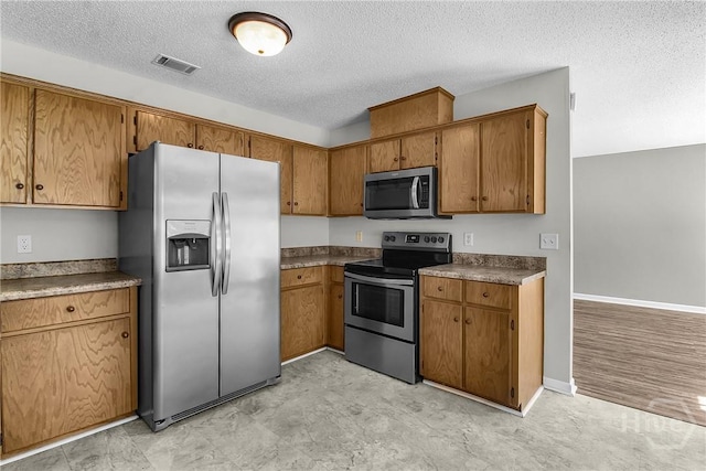 116 Gloucester Dr, Midway, GA 31320 - kitchen with stainless steel appliances, a textured ceiling, brown cabinetry, dark countertops, and light floors
