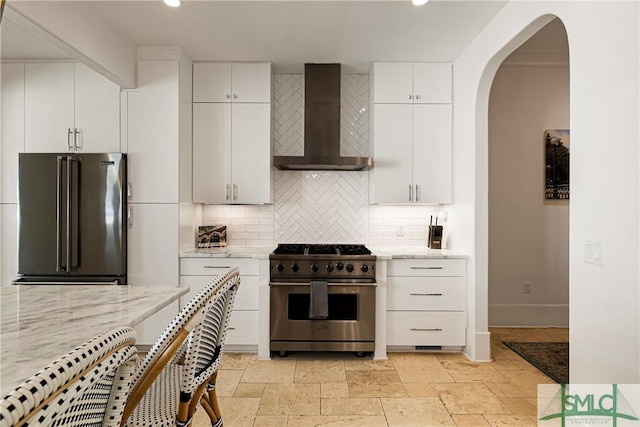 52-56 E Broad St, Savannah, GA 31401 - kitchen featuring high quality appliances, wall chimney exhaust hood, backsplash, arched walkways, and white cabinets