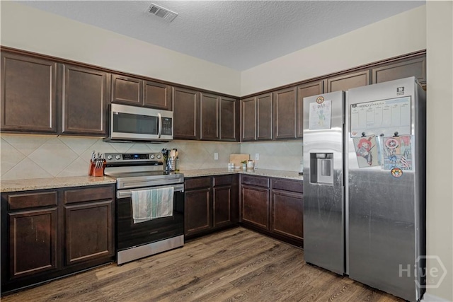 291 Morgan Field Blvd NE, Ludowici, GA 31316 - kitchen featuring appliances with stainless steel finishes, dark brown cabinets, wood finished floors, decorative backsplash, and light stone counters