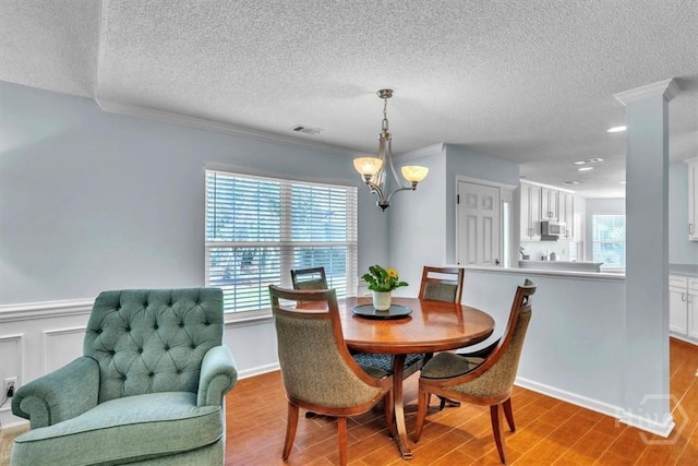 24 Marsh Hen Ct, Richmond Hill, GA 31324 - dining room featuring a chandelier, a textured ceiling, wood finished floors, crown molding, and a wainscoted wall
