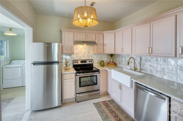 1136 E 39th St, Savannah, GA 31404 - kitchen featuring appliances with stainless steel finishes, under cabinet range hood, washer and dryer, a chandelier, and light countertops