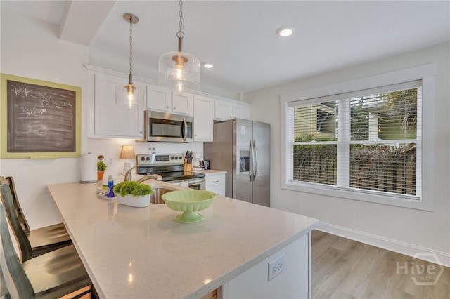 13 Izlar Ave, Tybee Island, GA 31328 - kitchen with appliances with stainless steel finishes, white cabinetry, a kitchen bar, decorative light fixtures, and light wood finished floors