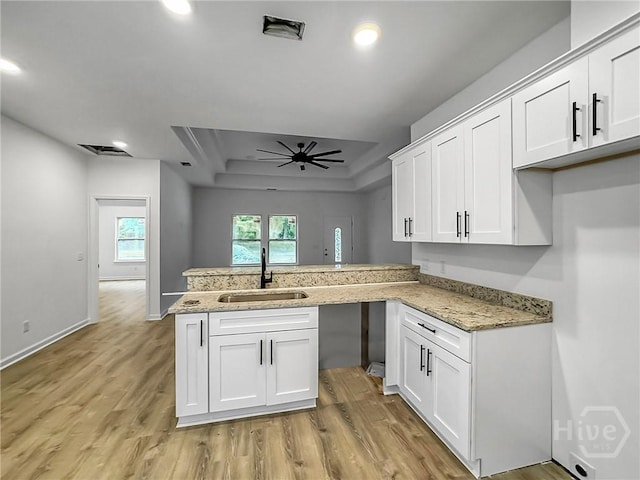 1031 Milton St, Savannah, GA 31405 - kitchen with a raised ceiling, a peninsula, light wood-style floors, white cabinets, and light stone counters