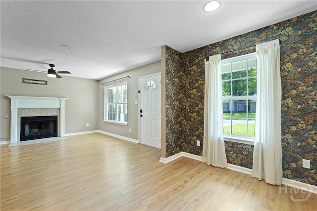 7305 Leghorn St, Savannah, GA 31406 - unfurnished living room with light wood-style flooring, a ceiling fan, a tile fireplace, wallpapered walls, and a textured ceiling