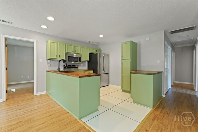 7305 Leghorn St, Savannah, GA 31406 - kitchen featuring green cabinetry, appliances with stainless steel finishes, wood counters, a peninsula, and light wood finished floors
