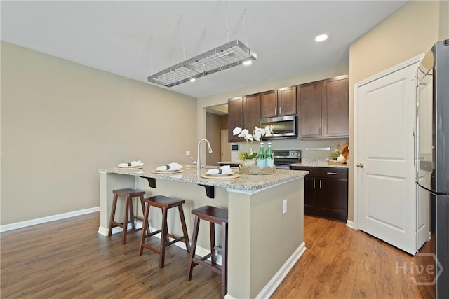 7 Saddle St N, Savannah, GA 31407 - kitchen featuring appliances with stainless steel finishes, a center island with sink, light wood-type flooring, dark brown cabinets, and a kitchen bar