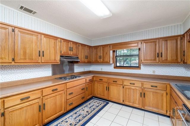 401 E Smith St, Claxton, GA 30417 - kitchen featuring wallpapered walls, stainless steel stovetop, under cabinet range hood, brown cabinetry, and light tile patterned floors