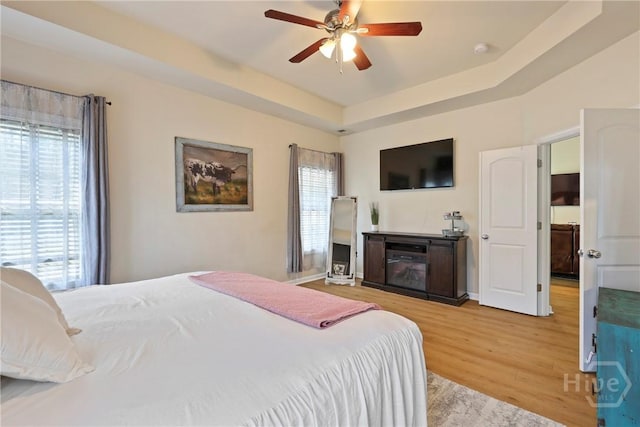 28 Cross Gate Ct, Pooler, GA 31322 - bedroom featuring light wood-style floors, a ceiling fan, a tray ceiling, and a glass covered fireplace