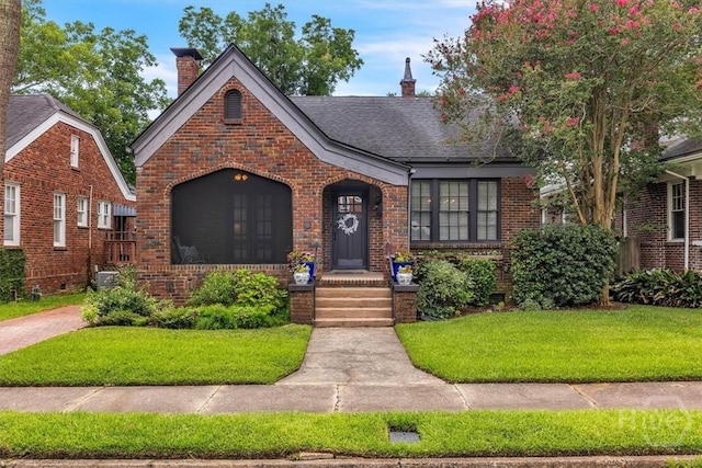 217 E 54th St, Savannah, GA 31405 - tudor home with brick siding, a chimney, a front yard, and roof with shingles