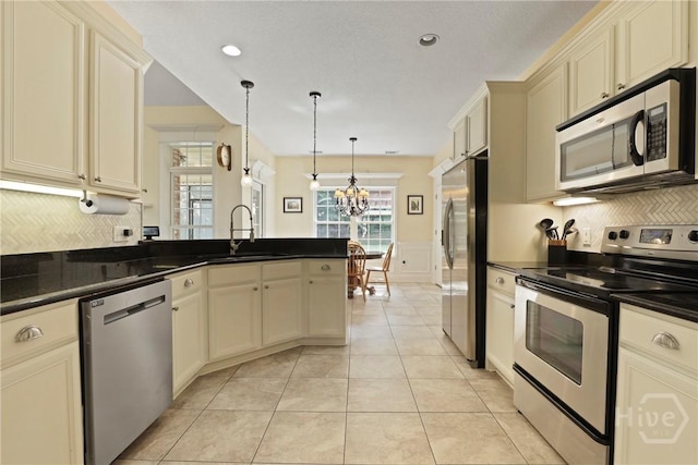 72 Roswell Trl, Richmond Hill, GA 31324 - kitchen with stainless steel appliances, cream cabinetry, a chandelier, dark countertops, and wainscoting