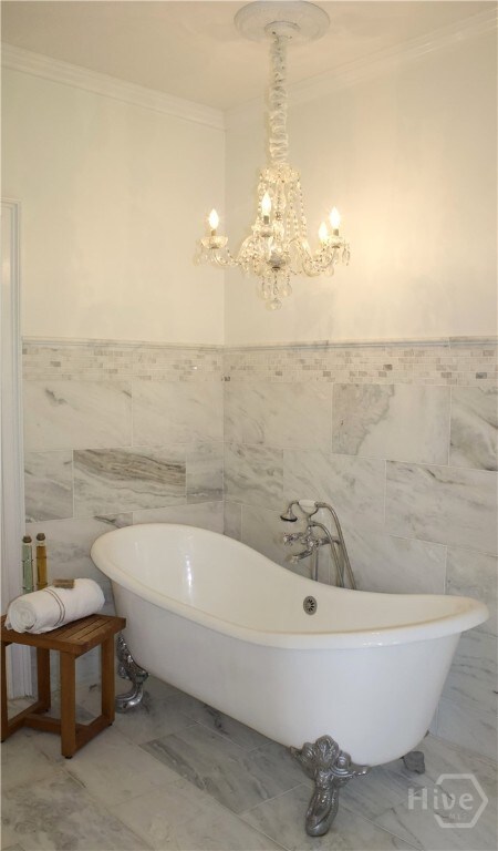 2766 Fort Mcallister Rd, Richmond Hill, GA 31324 - full bathroom featuring ornamental molding, tile walls, a chandelier, marble finish floors, and a freestanding bath