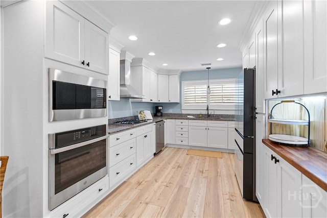 115 Coquena Cir E, Savannah, GA 31410 - kitchen featuring appliances with stainless steel finishes, wall chimney range hood, light wood-style flooring, white cabinets, and recessed lighting