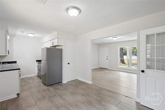 1021 Walnut Ct, Springfield, GA 31329 - kitchen with freestanding refrigerator, white cabinets, a textured ceiling, dark countertops, and wood finished floors