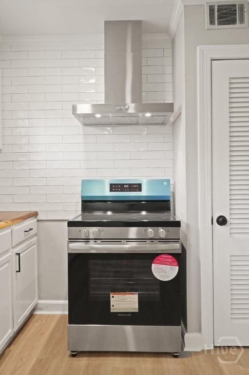 13 Hughes Ave, Savannah, GA 31406 - kitchen with stainless steel electric stove, wall chimney exhaust hood, ornamental molding, white cabinets, and light wood finished floors