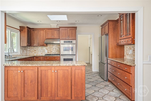 1 Hobcaw Ln, Savannah, GA 31411 - kitchen featuring appliances with stainless steel finishes, under cabinet range hood, brown cabinets, a peninsula, and crown molding