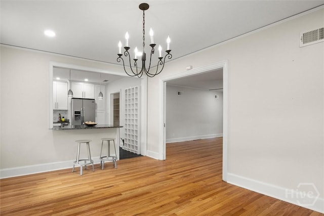 540 E 60th St, Savannah, GA 31405 - kitchen featuring stainless steel refrigerator with ice dispenser, white cabinetry, light wood-type flooring, a breakfast bar area, and a chandelier
