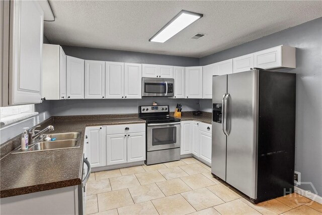 65 Fabian Ln, Hinesville, GA 31313 - kitchen featuring stainless steel appliances, dark countertops, a textured ceiling, white cabinets, and light tile patterned flooring