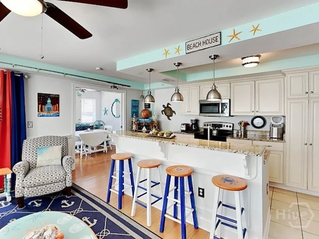 1415 Butler Ave Unit 1, Tybee Island, GA 31328 - kitchen with range, stainless steel microwave, a kitchen breakfast bar, a ceiling fan, and light stone counters